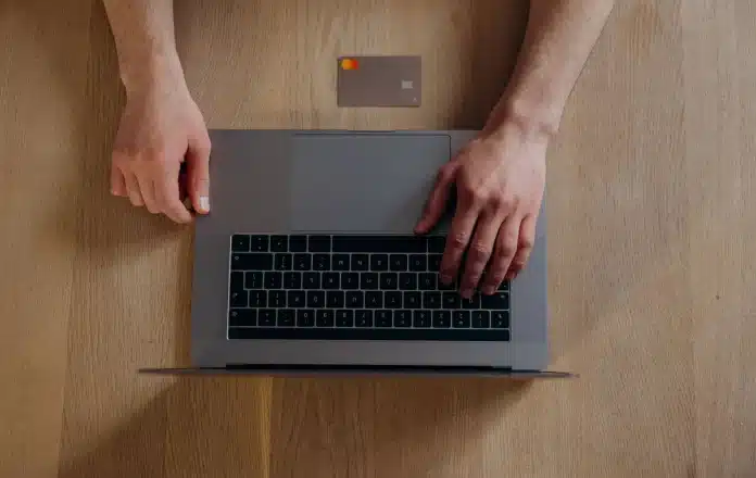 Personne testant une plateforme e-commerce sur ordinateur avec documents de planification Personne testant une plateforme e-commerce sur ordinateur avec documents de planification
